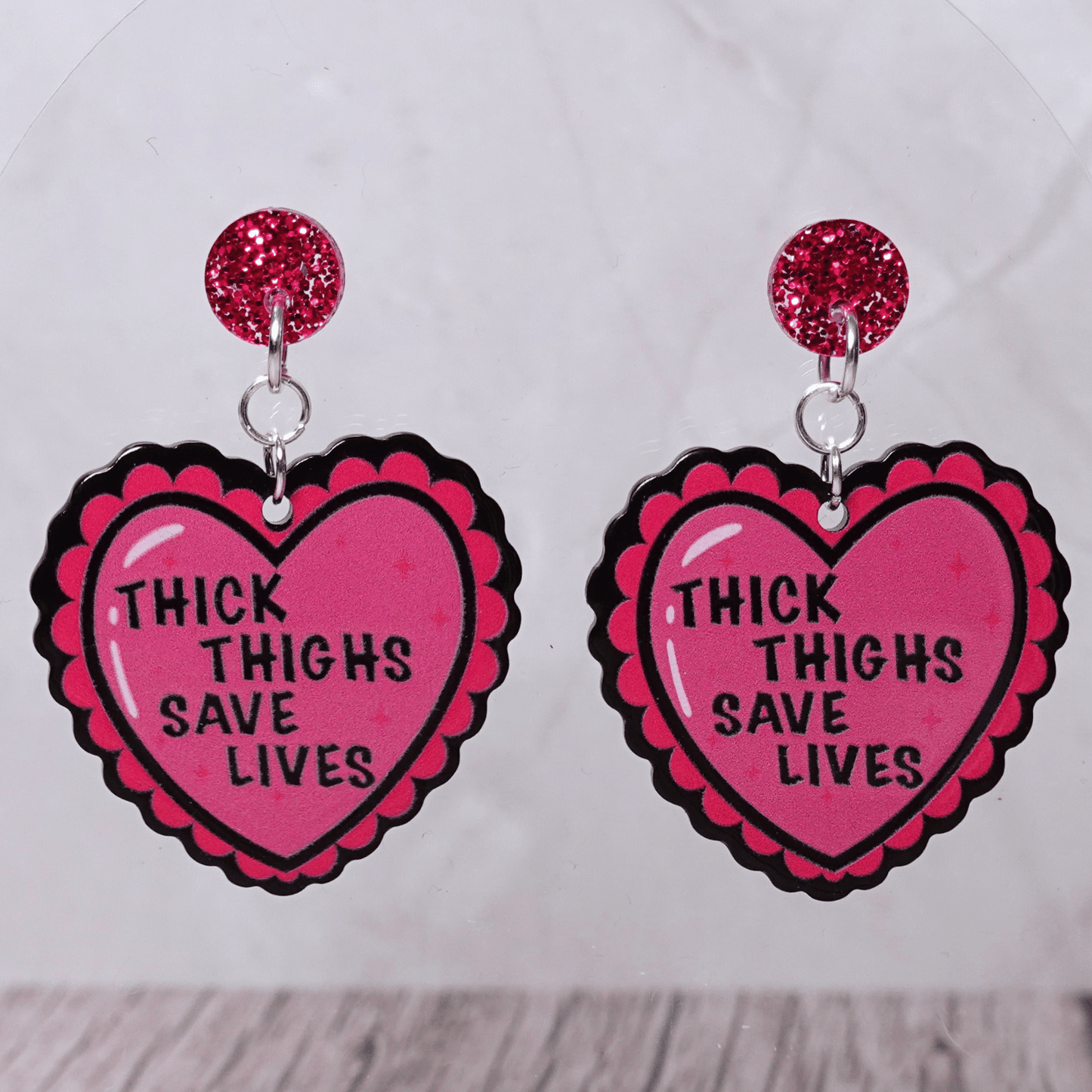 Pink heart dangle earrings with text “thick thighs save lives” and glitter stud tops