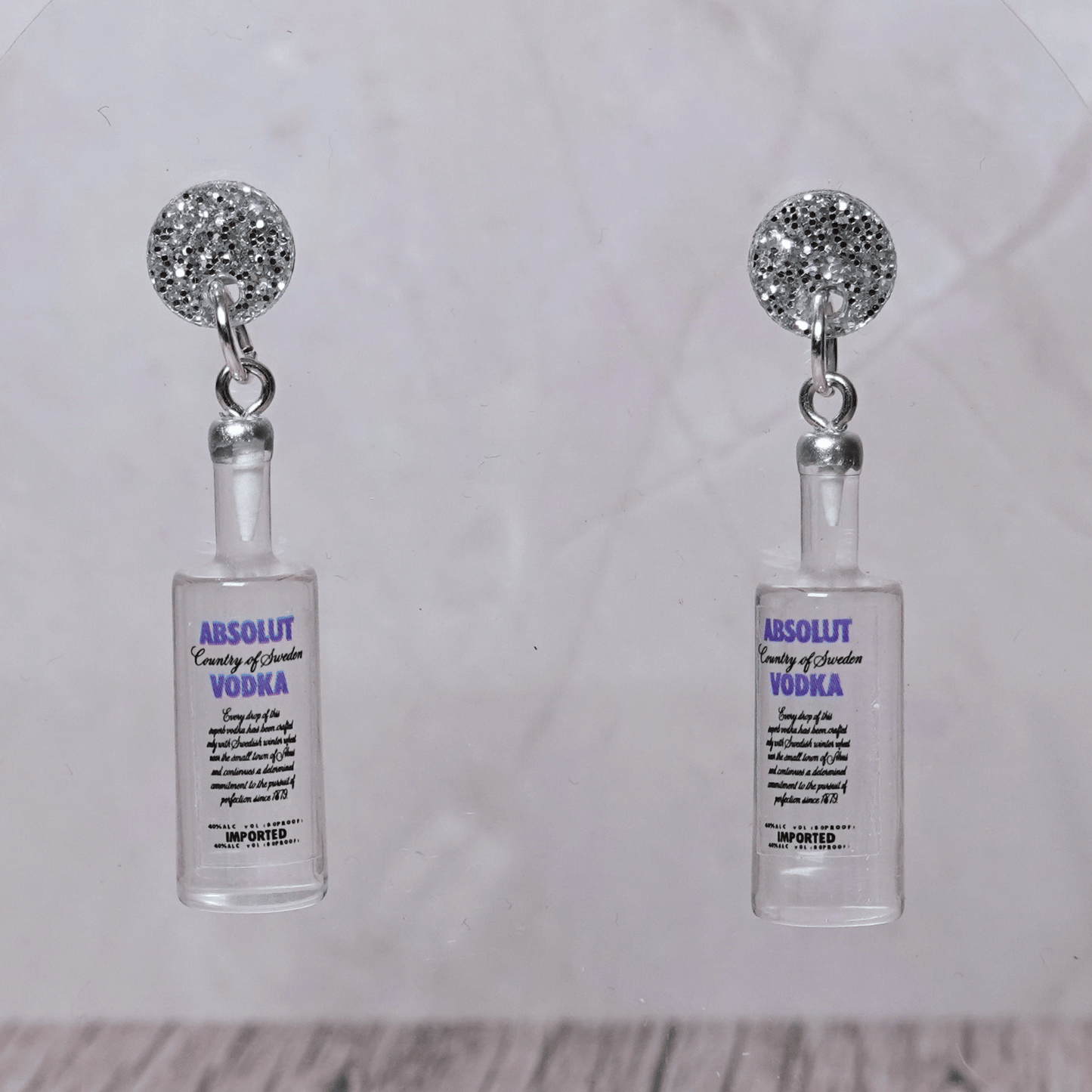 Novelty dangle earrings shaped like clear vodka bottles with a printed vodka-style label design.