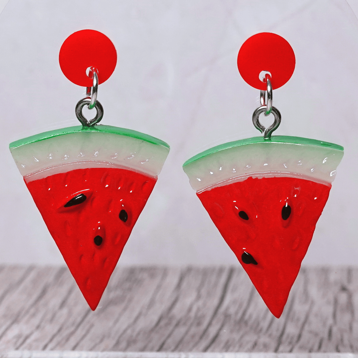 Watermelon slice dangle earrings shaped like red triangular watermelon pieces with green rind and black seed details on red stud tops
