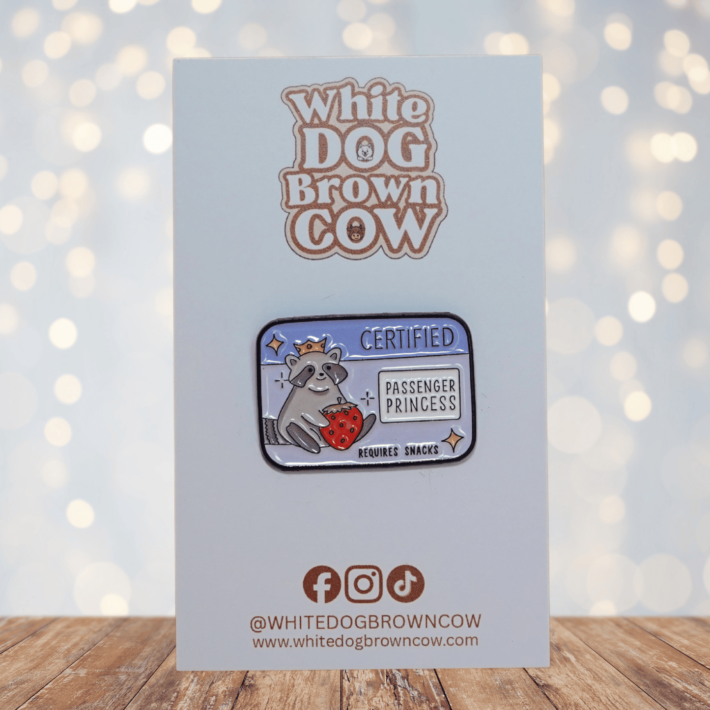 Raccoon enamel pin wearing a crown, holding a strawberry, with text “Certified Passenger Princess – Requires Snacks.”