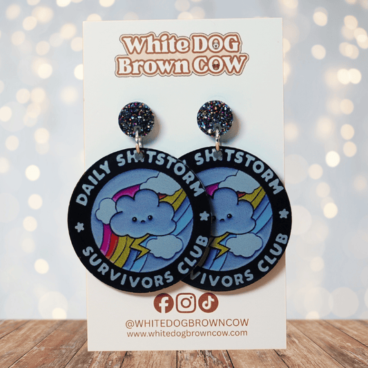 Round novelty dangle earrings reading “Daily Shitstorm Survivors Club” with a cute cloud, rainbow and lightning design