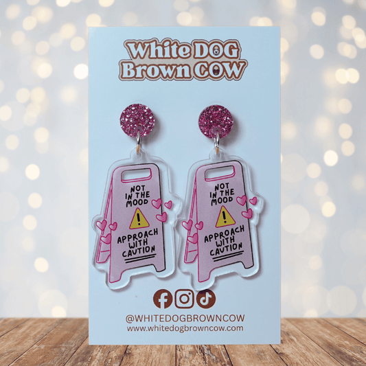 Funny acrylic dangle earrings shaped like a caution sign that reads “Not in the mood – approach with caution,” decorated with small pink hearts.