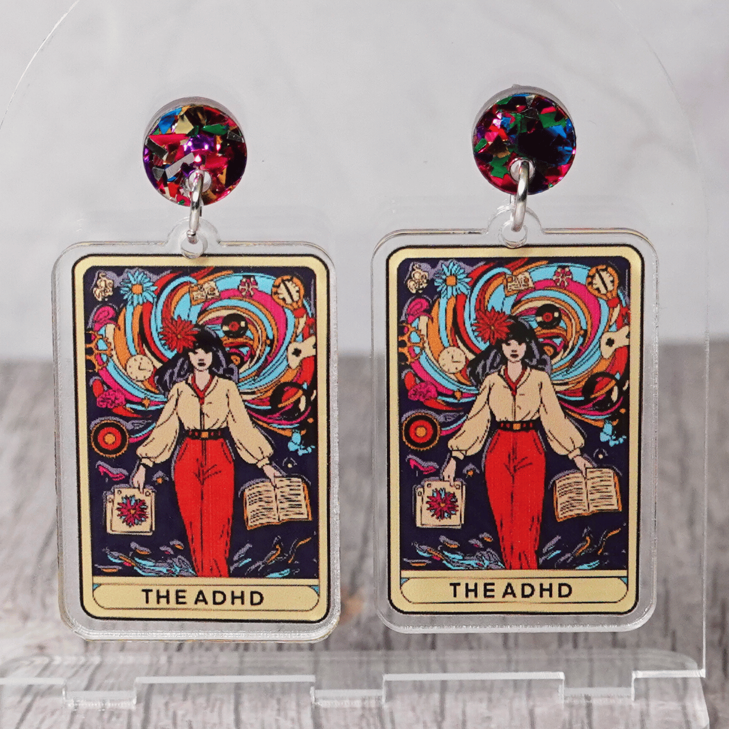 Acrylic dangle earrings featuring a colorful tarot-style card labeled “The ADHD” with a woman surrounded by swirling patterns and books.