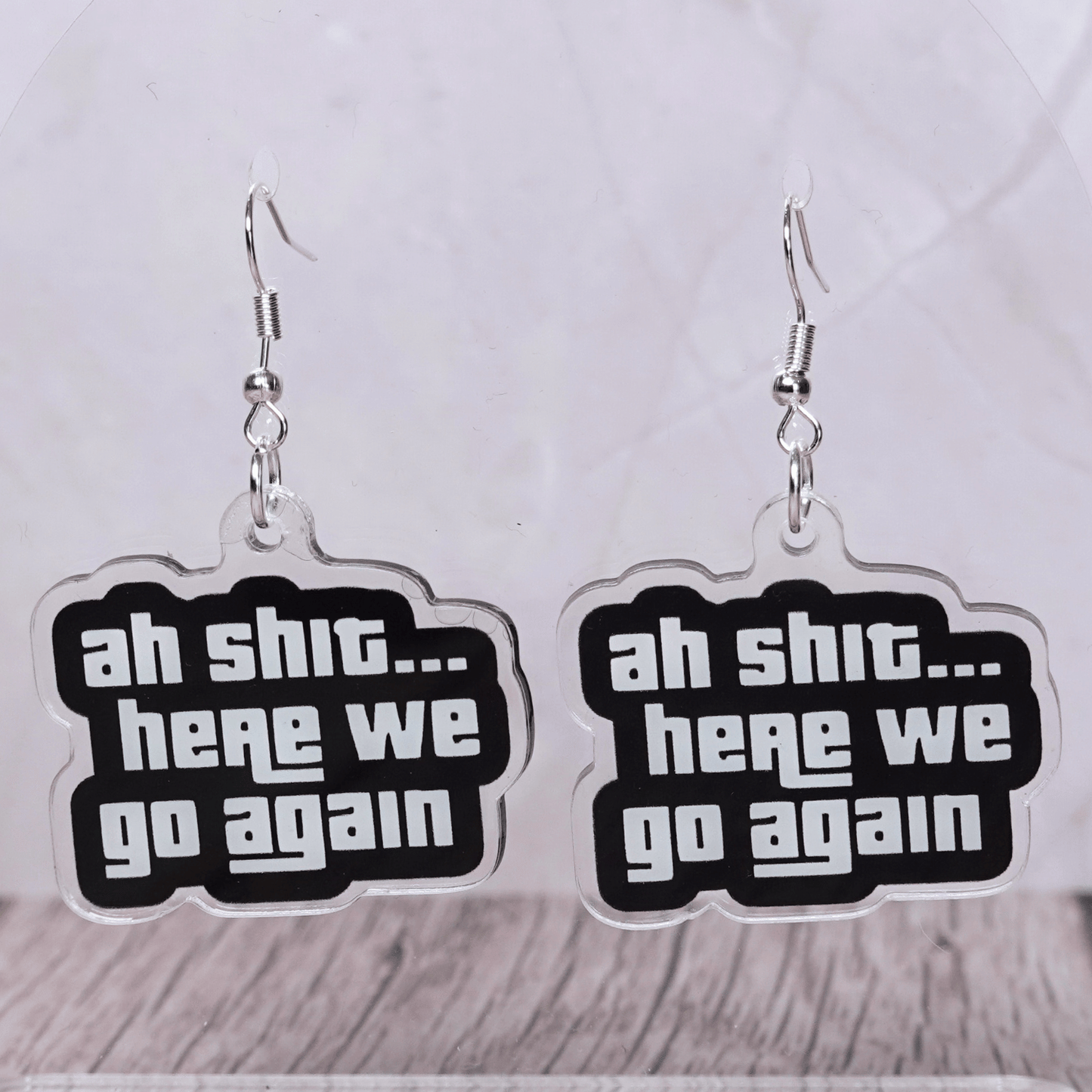 Black and white novelty earrings with text “ah shit here we go again”