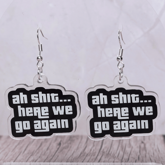 Black and white novelty earrings with text “ah shit here we go again”
