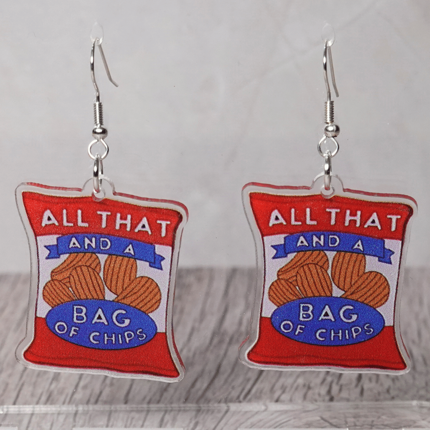 Acrylic dangle earrings shaped like a red potato chip bag that reads “All That and a Bag of Chips,” featuring illustrated chips and bold retro lettering.