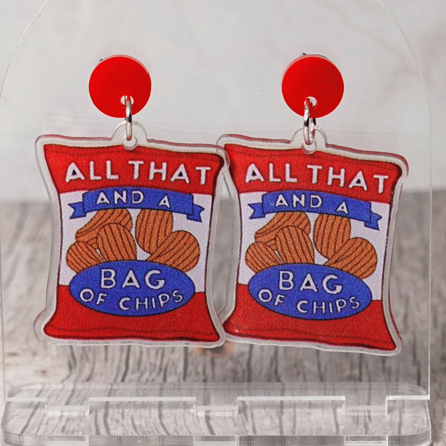 Acrylic dangle earrings shaped like a red potato chip bag that reads “All That and a Bag of Chips,” featuring illustrated chips and bold retro lettering.