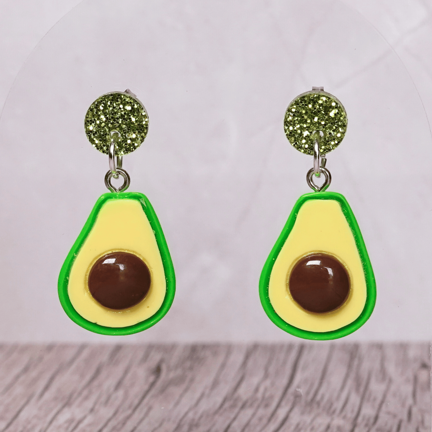 Avocado shaped dangle earrings with green outline, pale yellow center and raised brown pit on glitter studs