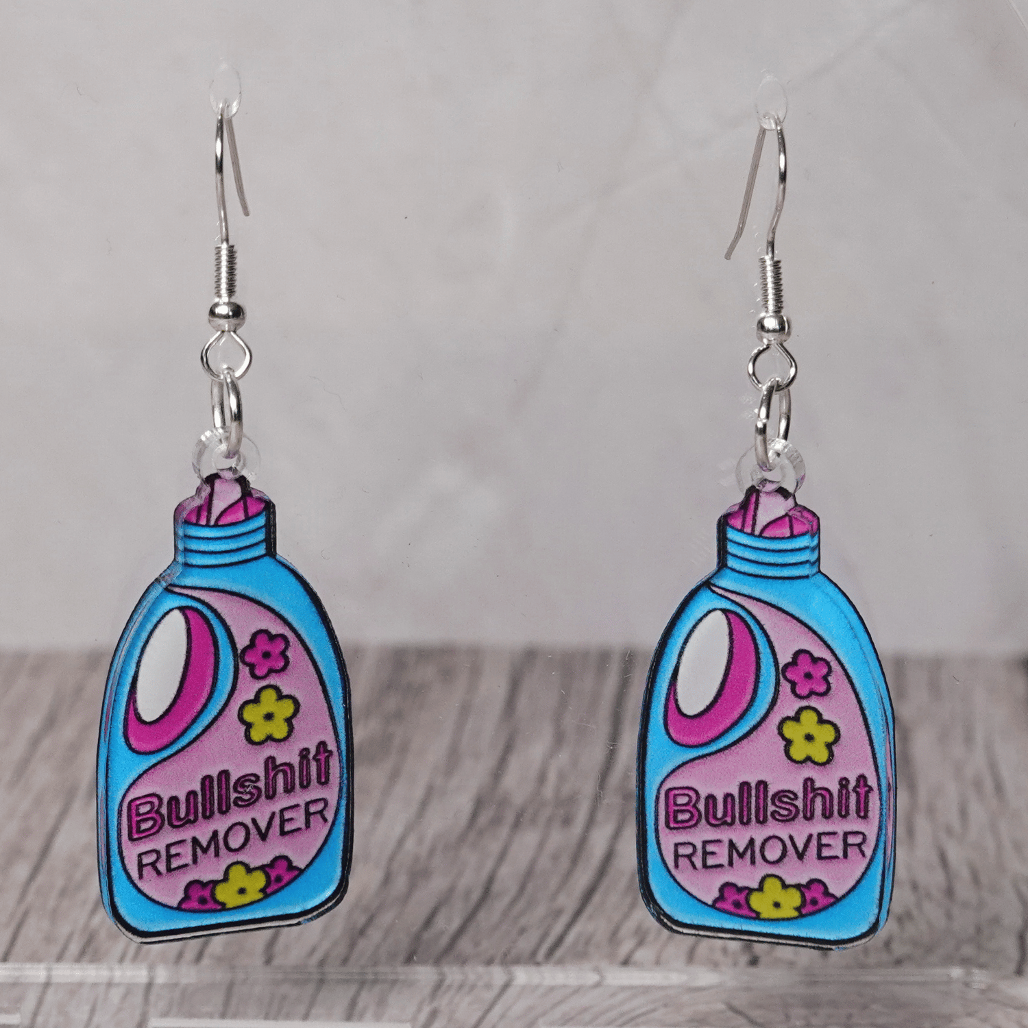 Colorful novelty dangle earrings shaped like a detergent bottle labeled “Bullsh*t remover”