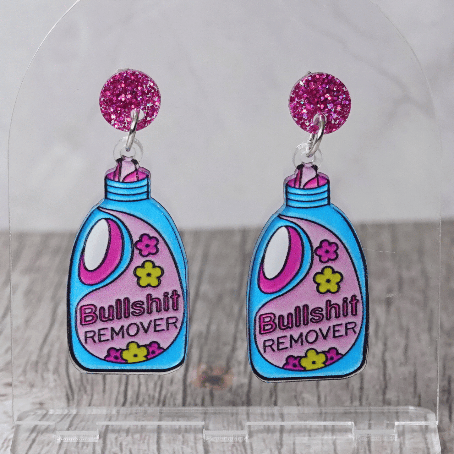 Colorful novelty dangle earrings shaped like a detergent bottle labeled “Bullsh*t remover” with glitter stud tops