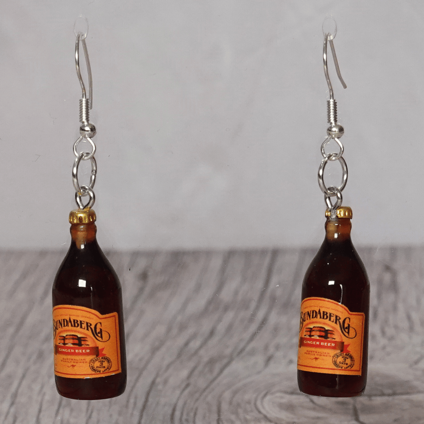 Mini brown ginger beer bottle shaped dangle earrings with orange labels and silver hooks.