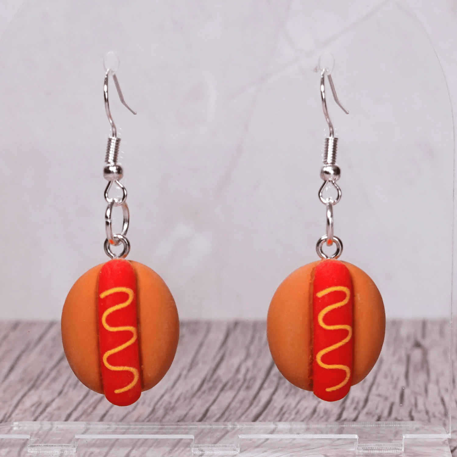 Novelty hot dog dangle earrings shaped like mini hot dogs with mustard detail on a bun and silver hooks.