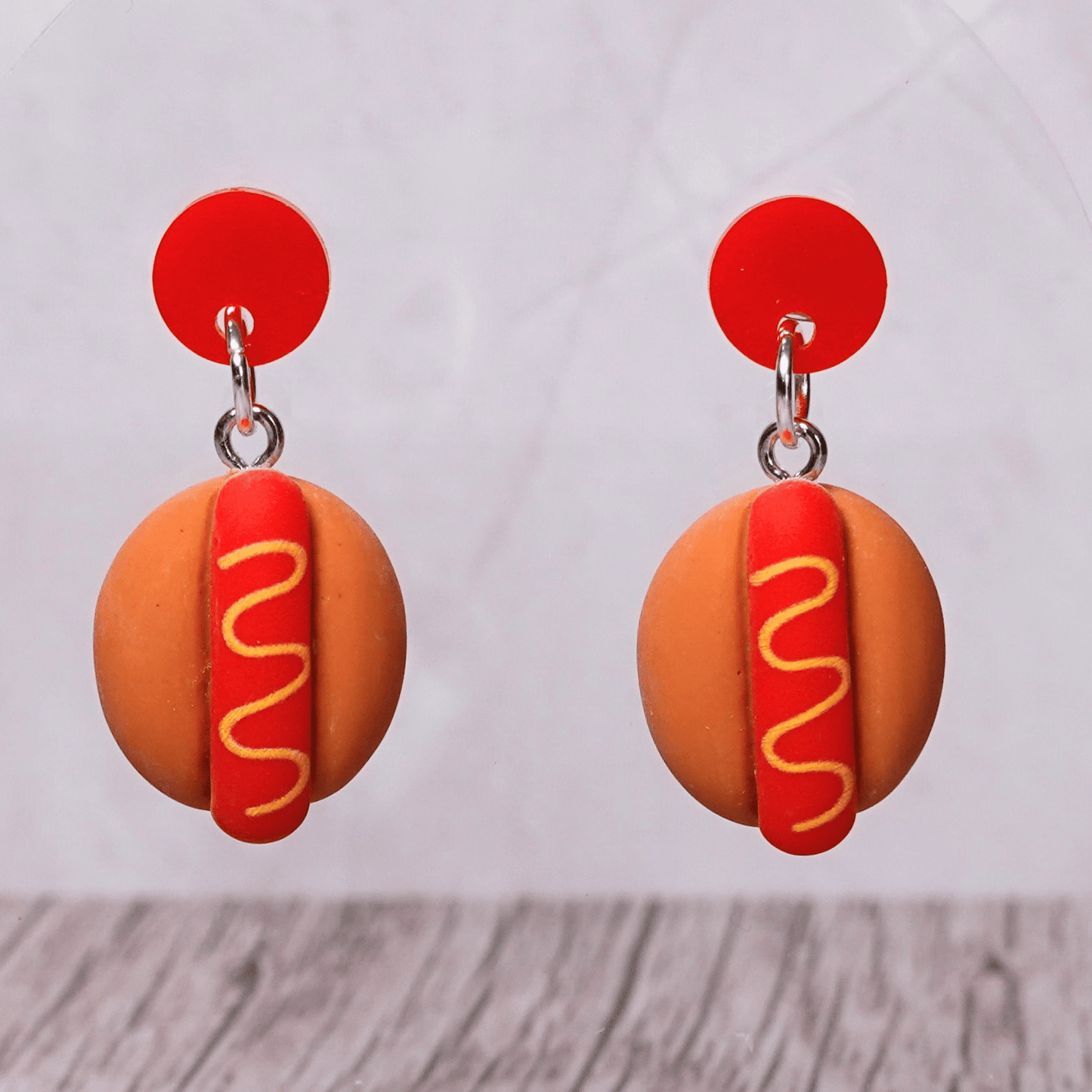 Novelty hot dog dangle earrings shaped like mini hot dogs with mustard detail on a bun and red studs