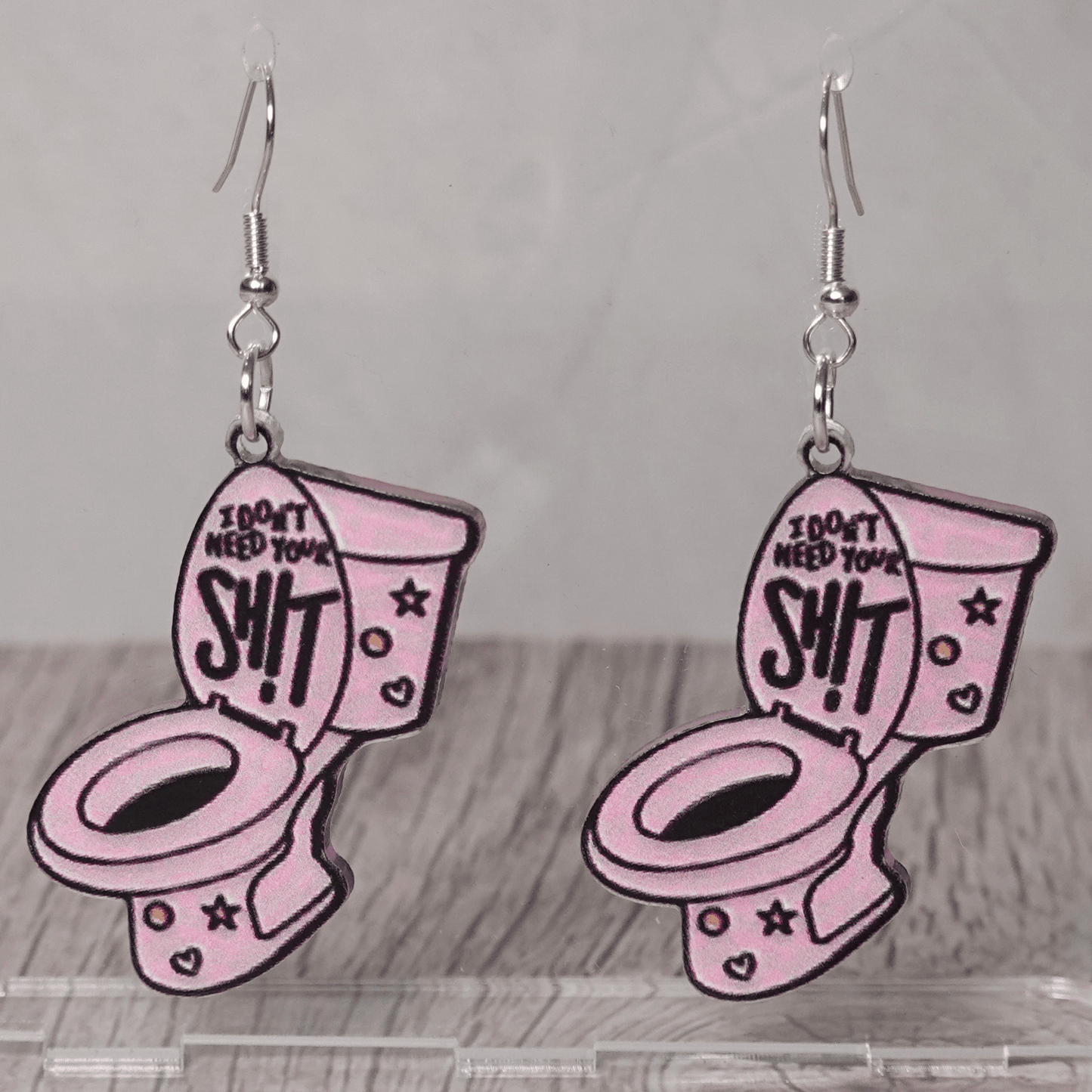 Pink novelty dangle earrings shaped like a toilet with text “I don’t need your sh*t”