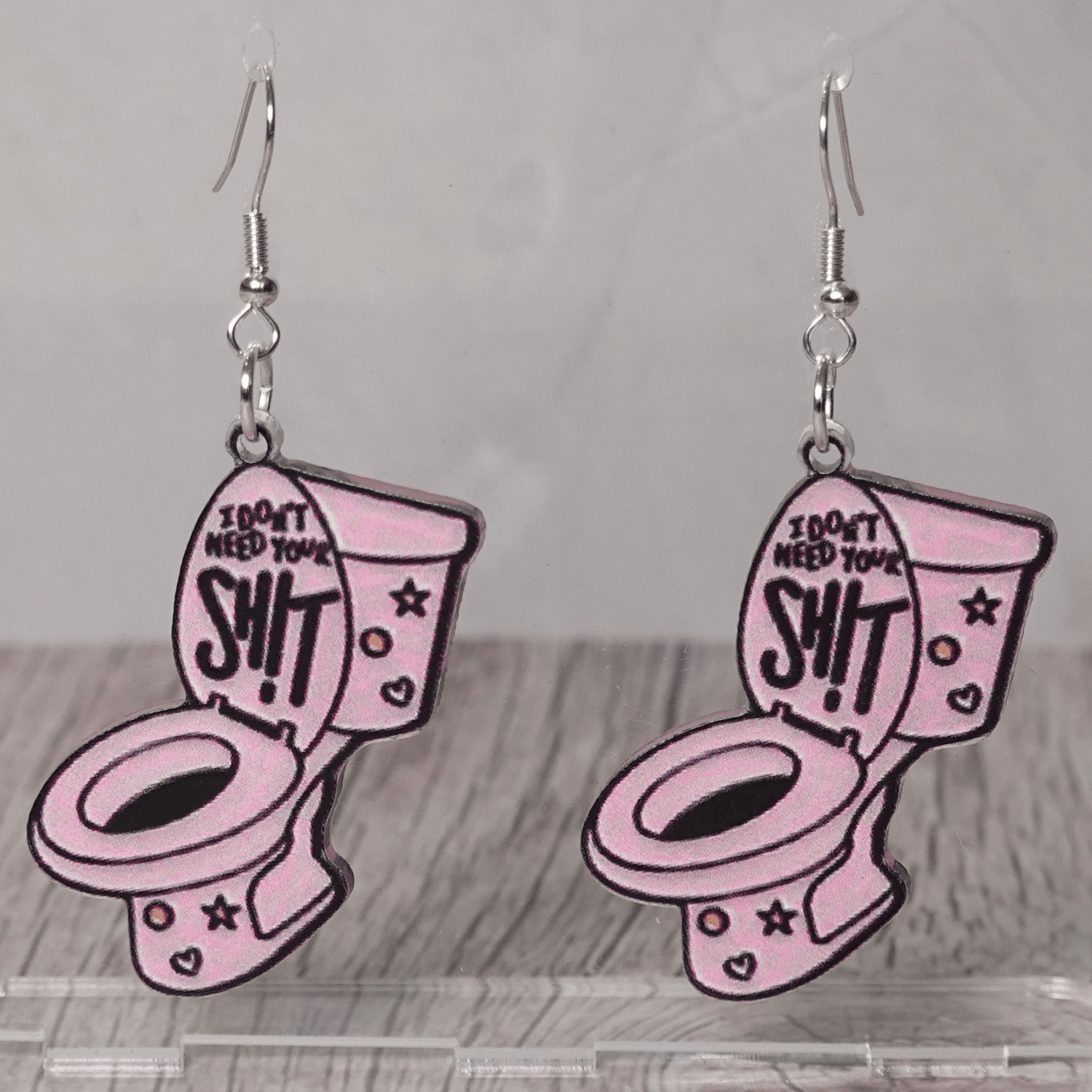 Pink novelty dangle earrings shaped like a toilet with text “I don’t need your sh*t”
