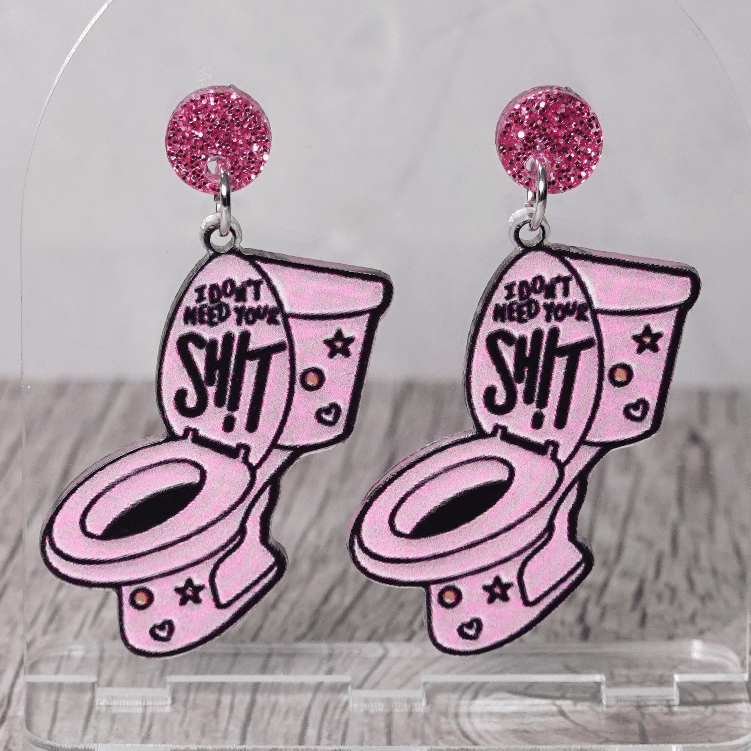 Pink novelty dangle earrings shaped like a toilet with text “I don’t need your sh*t” and glitter stud tops
