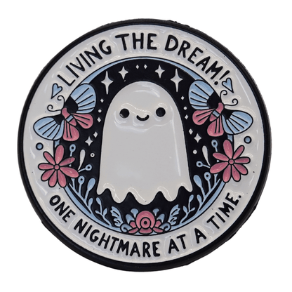 Cute ghost enamel pin with flowers and text “living the dream one nightmare at a time,” funny sarcastic spooky pin