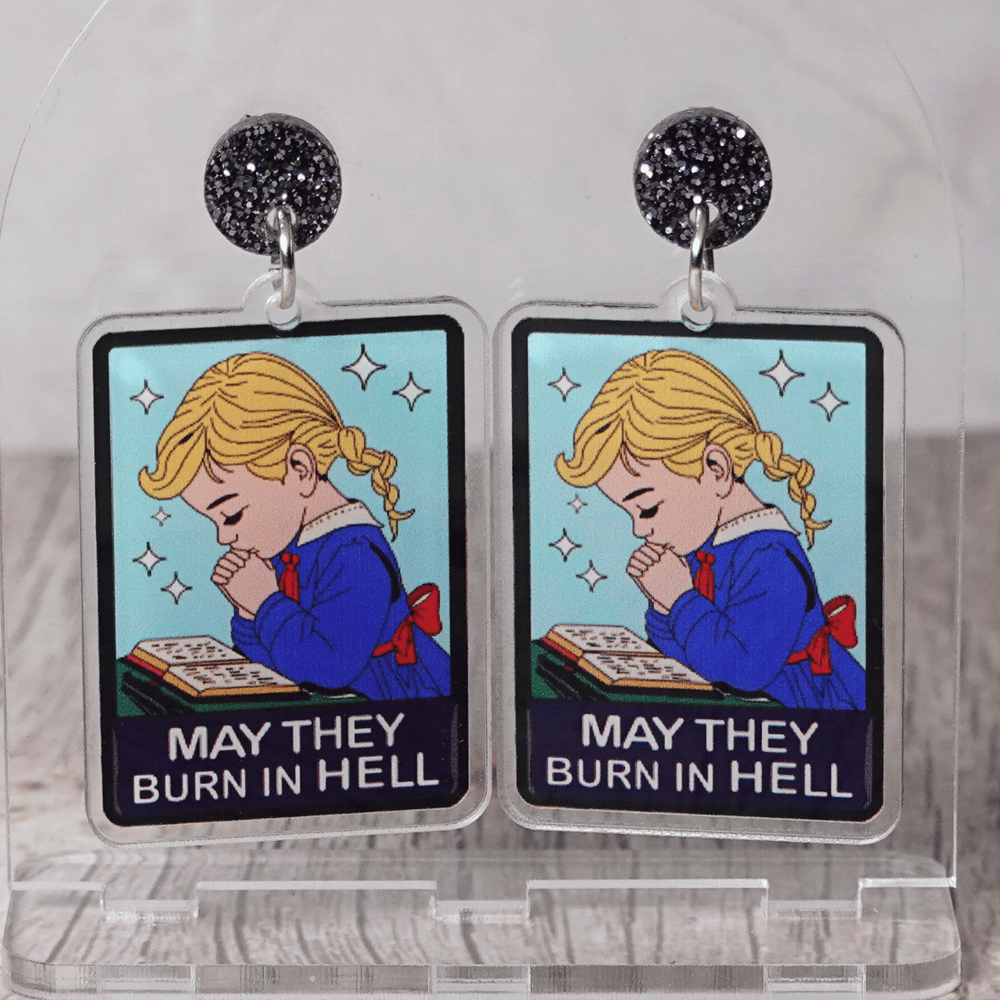 Clear acrylic dangle earrings with a vintage illustration of a praying girl and text reading “May they burn in hell”