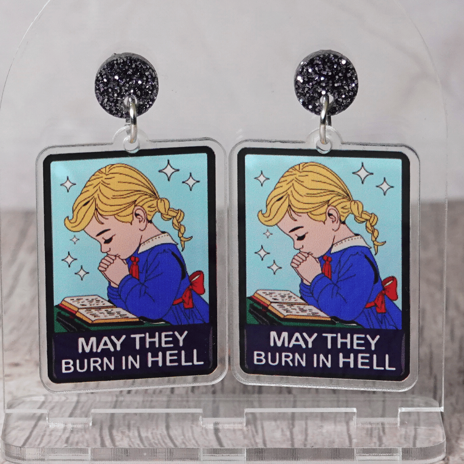 Clear acrylic dangle earrings with a vintage illustration of a praying girl and text reading “May they burn in hell”
