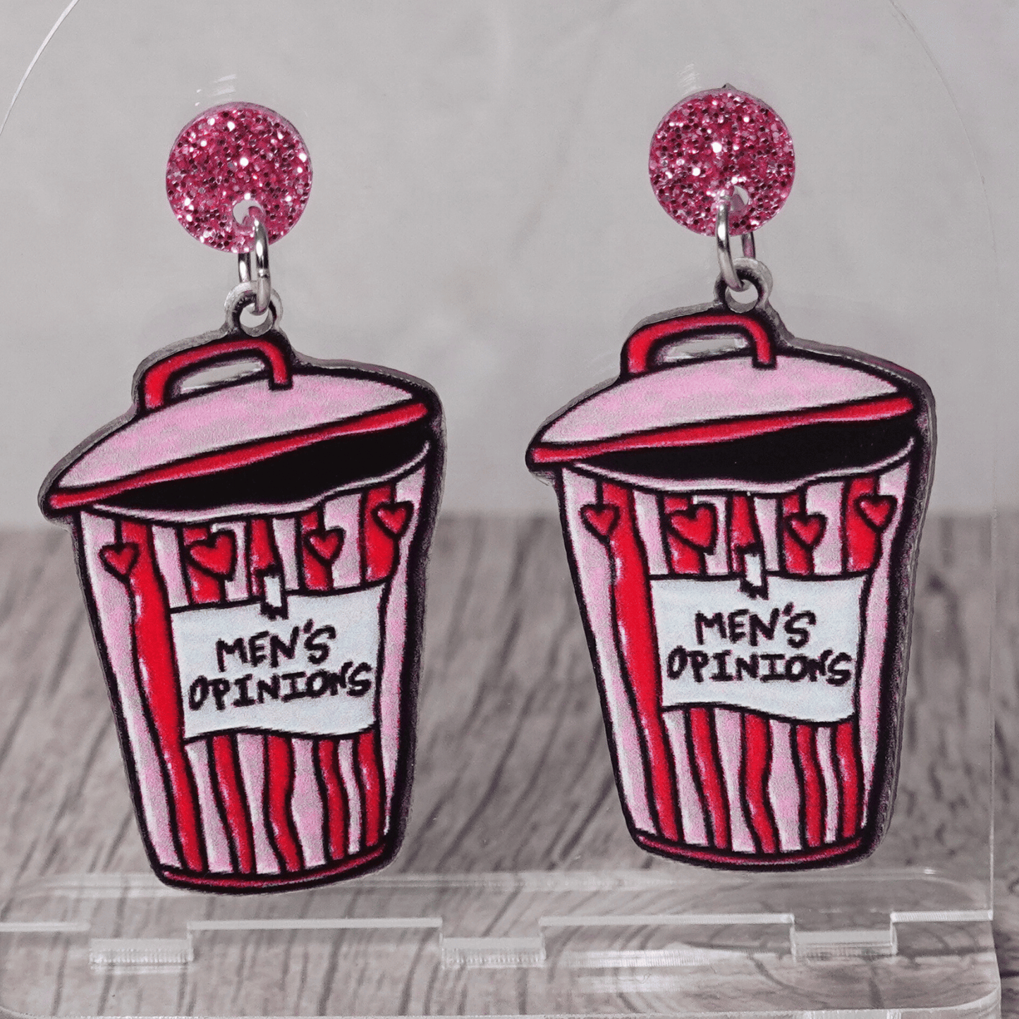 Acrylic dangle earrings shaped like a pink and red trash can labeled “Men’s Opinions”