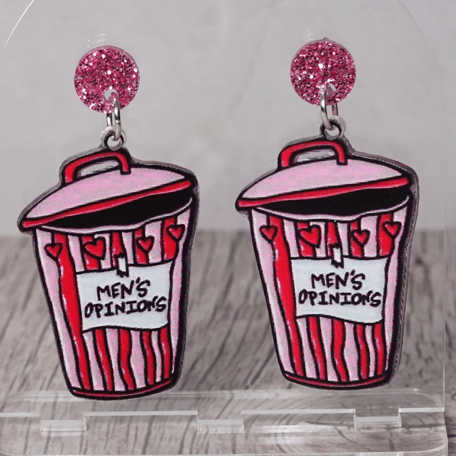 Acrylic dangle earrings shaped like a pink and red trash can labeled “Men’s Opinions”