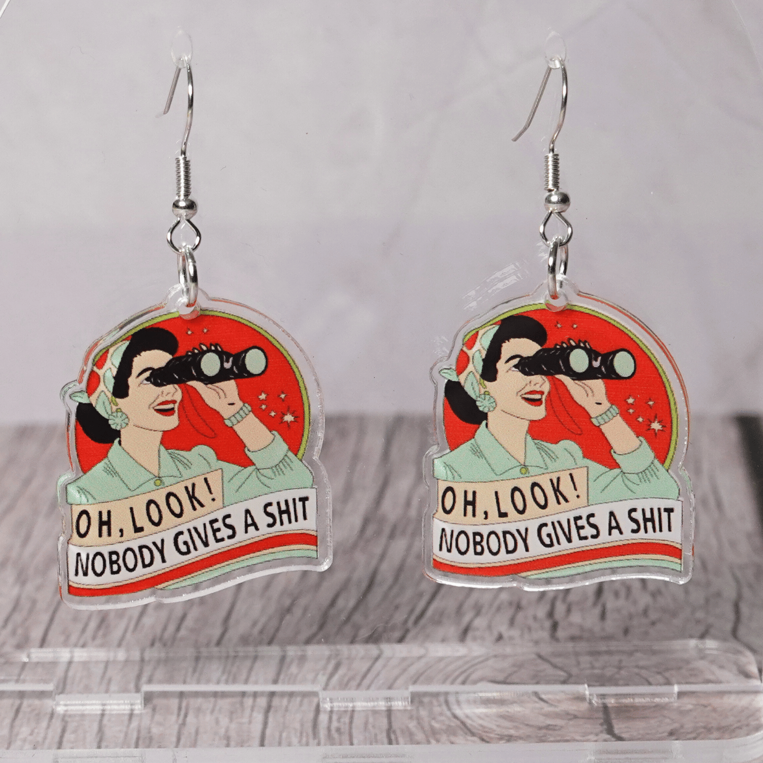 Retro style novelty dangle earrings showing a woman with binoculars and the phrase “Oh look nobody gives a sh*t”