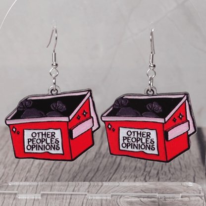 Acrylic dangle earrings shaped like a red dumpster labeled “Other People’s Opinions” with trash bags inside