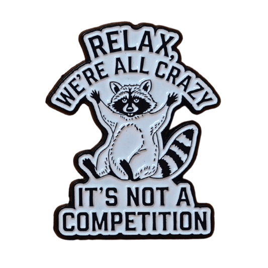Black and white enamel pin with raccoon illustration and quote “Relax, We’re All Crazy, It’s Not a Competition,” funny sarcastic lapel pin.