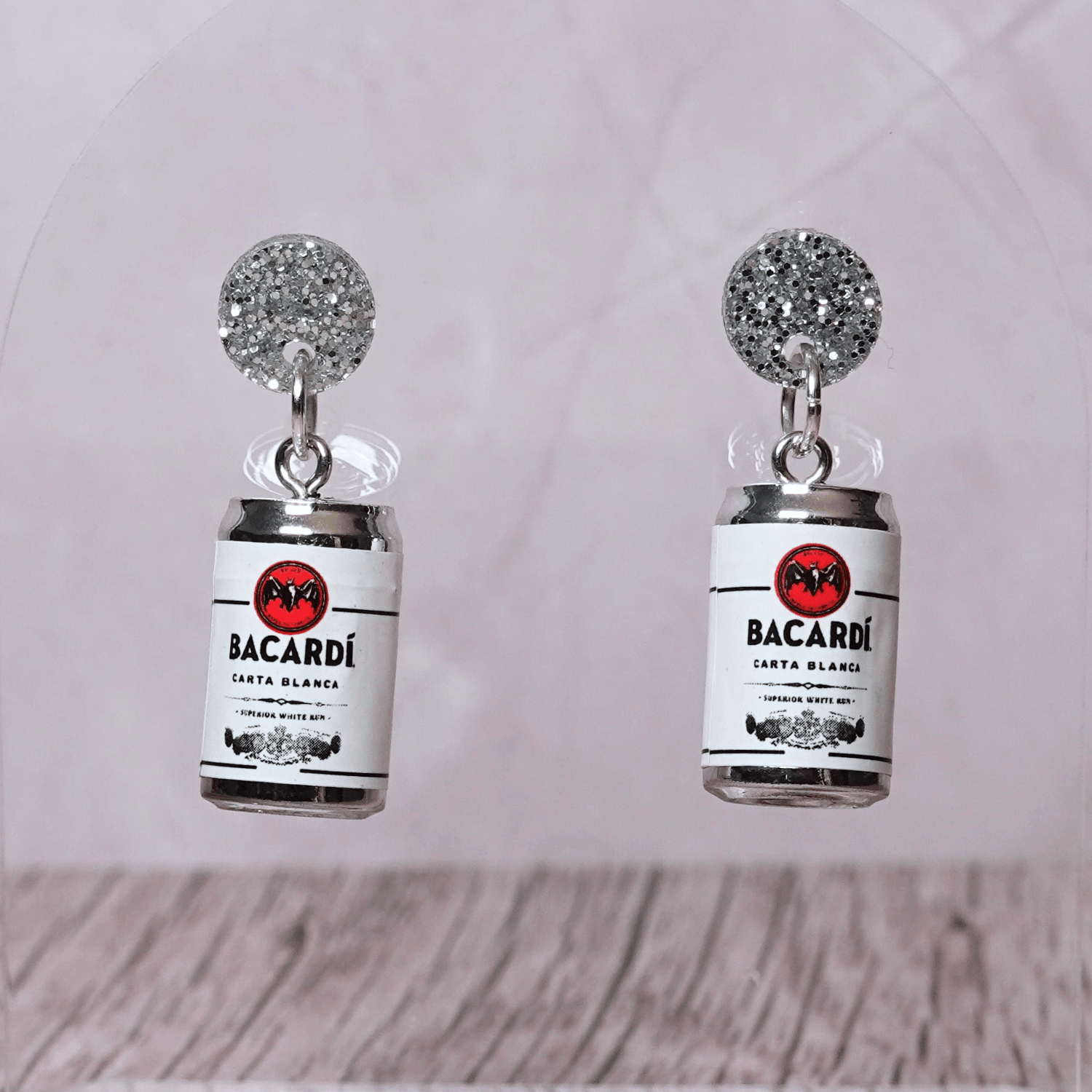 Novelty dangle earrings shaped like mini bacardi white rum cans with a printed label design and silver glitter studs.