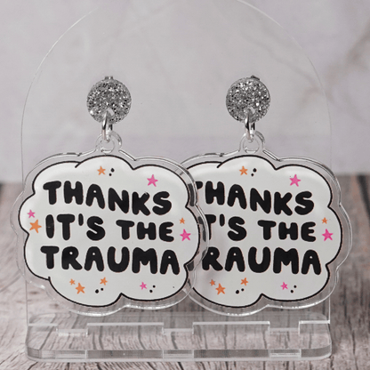 Clear acrylic dangle earrings with a speech bubble shape reading “Thanks it’s the trauma” with small star accents
