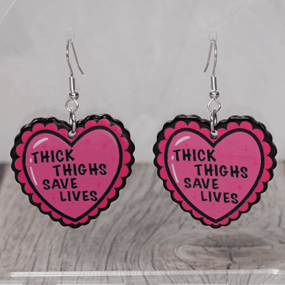 Pink heart dangle earrings with text “thick thighs save lives”