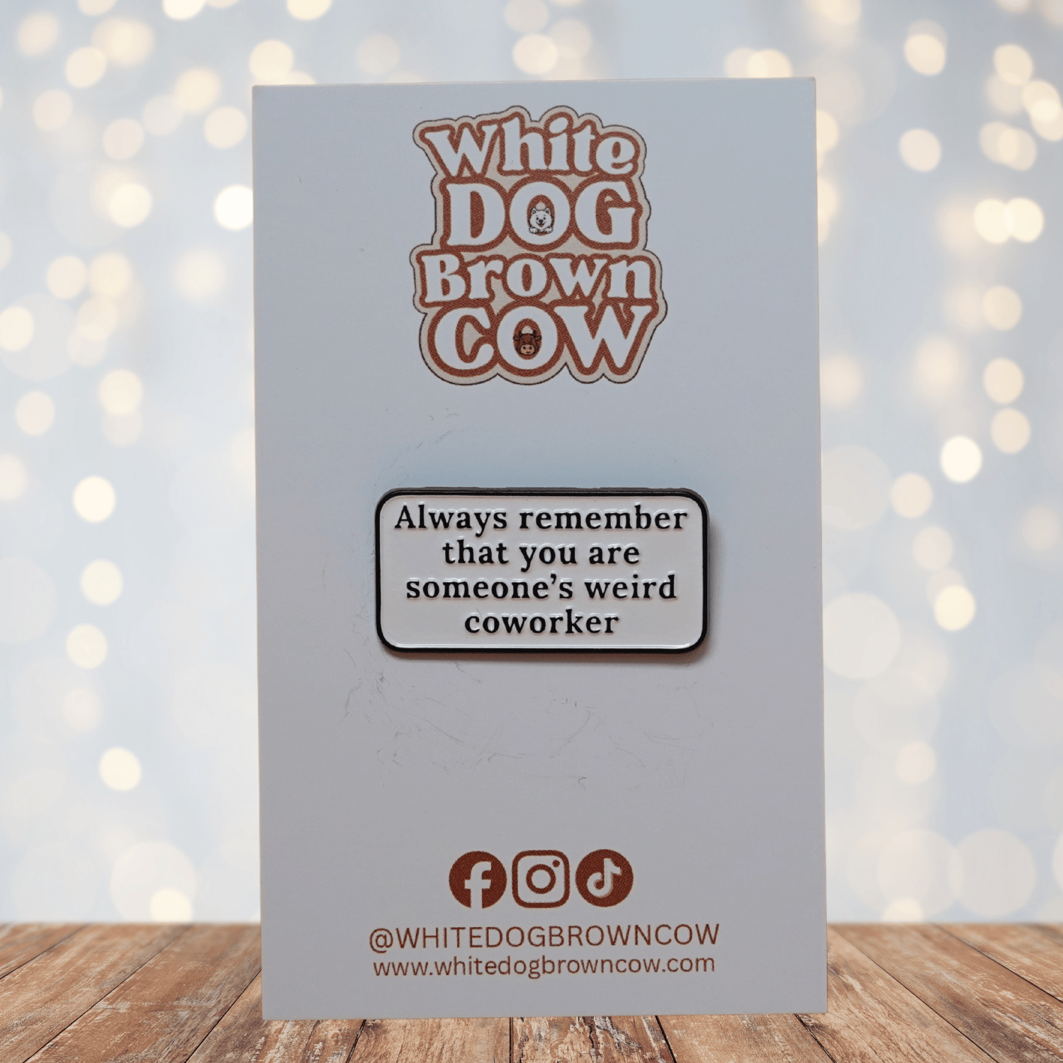 Rectangular enamel pin with the quote “Always remember that you are someone’s weird coworker” in black text on a white background.
