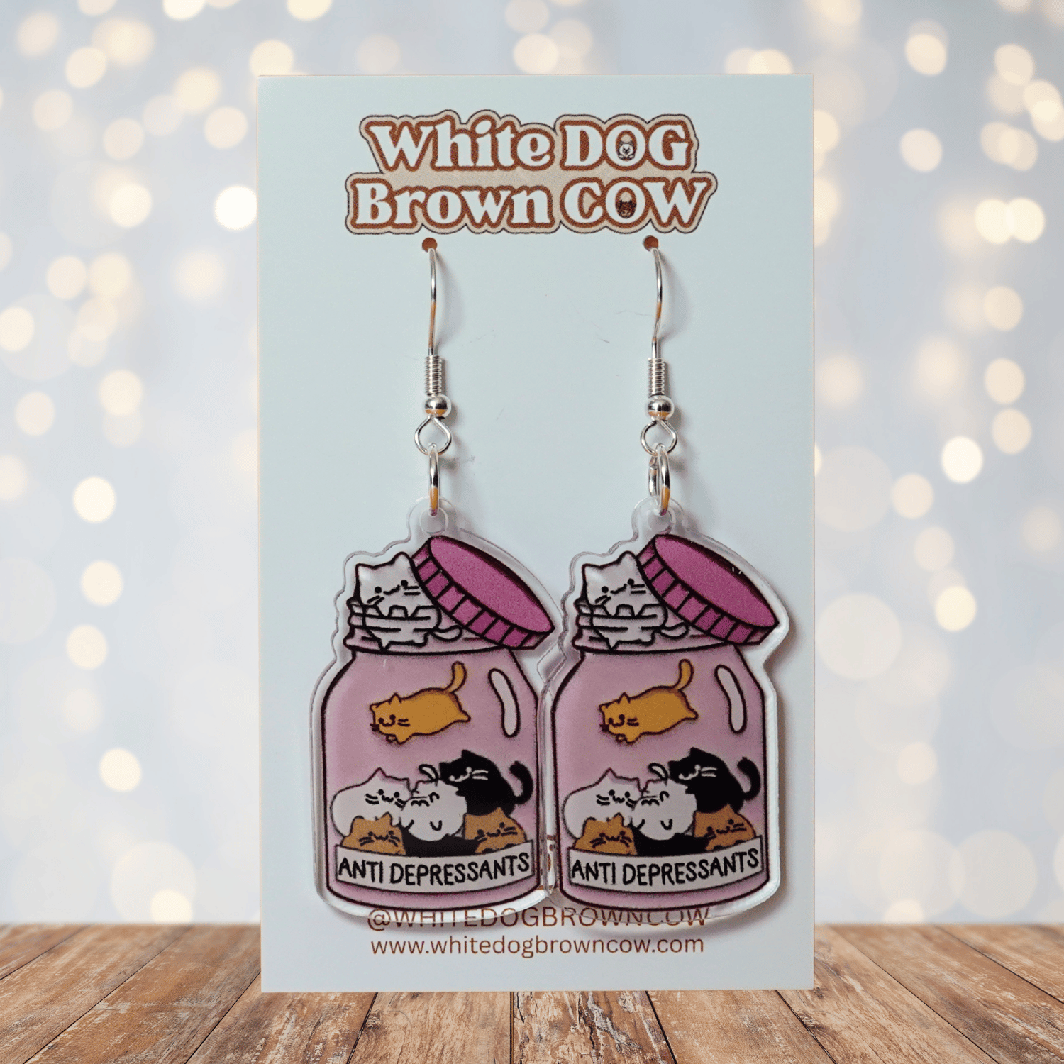 Acrylic dangle earrings shaped like a pink jar labeled “anti-depressants” filled with cartoon cats.