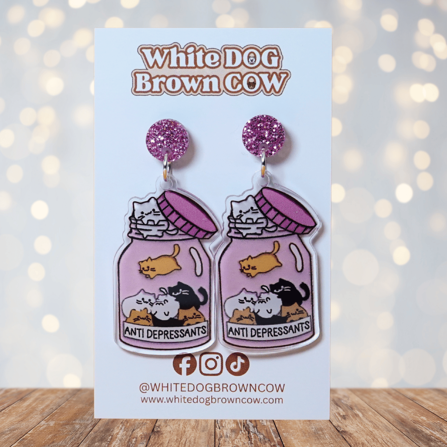 Acrylic dangle earrings shaped like a pink jar labeled “anti-depressants” filled with cartoon c