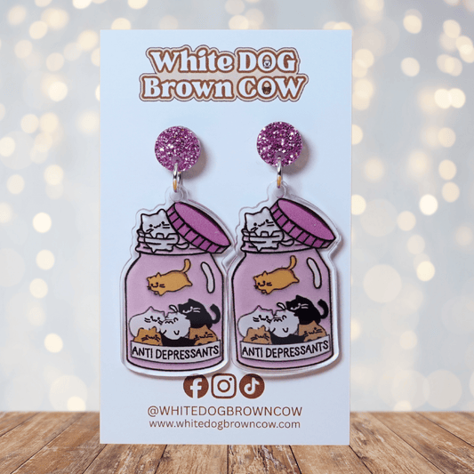 Acrylic dangle earrings shaped like a pink jar labeled “anti-depressants” filled with cartoon c