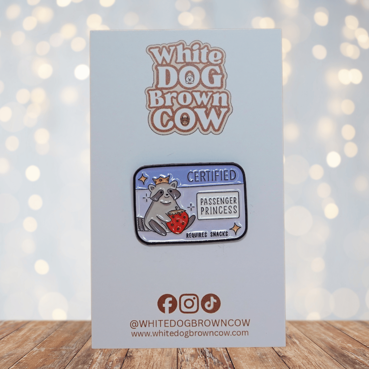 Raccoon enamel pin wearing a crown, holding a strawberry, with text “Certified Passenger Princess – Requires Snacks.”