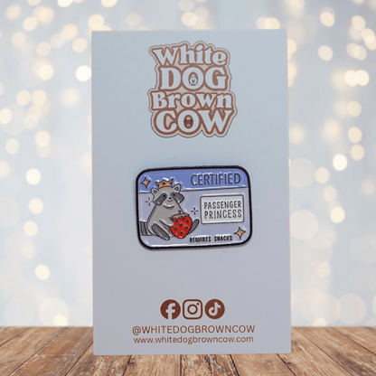 Raccoon enamel pin wearing a crown, holding a strawberry, with text “Certified Passenger Princess – Requires Snacks.”