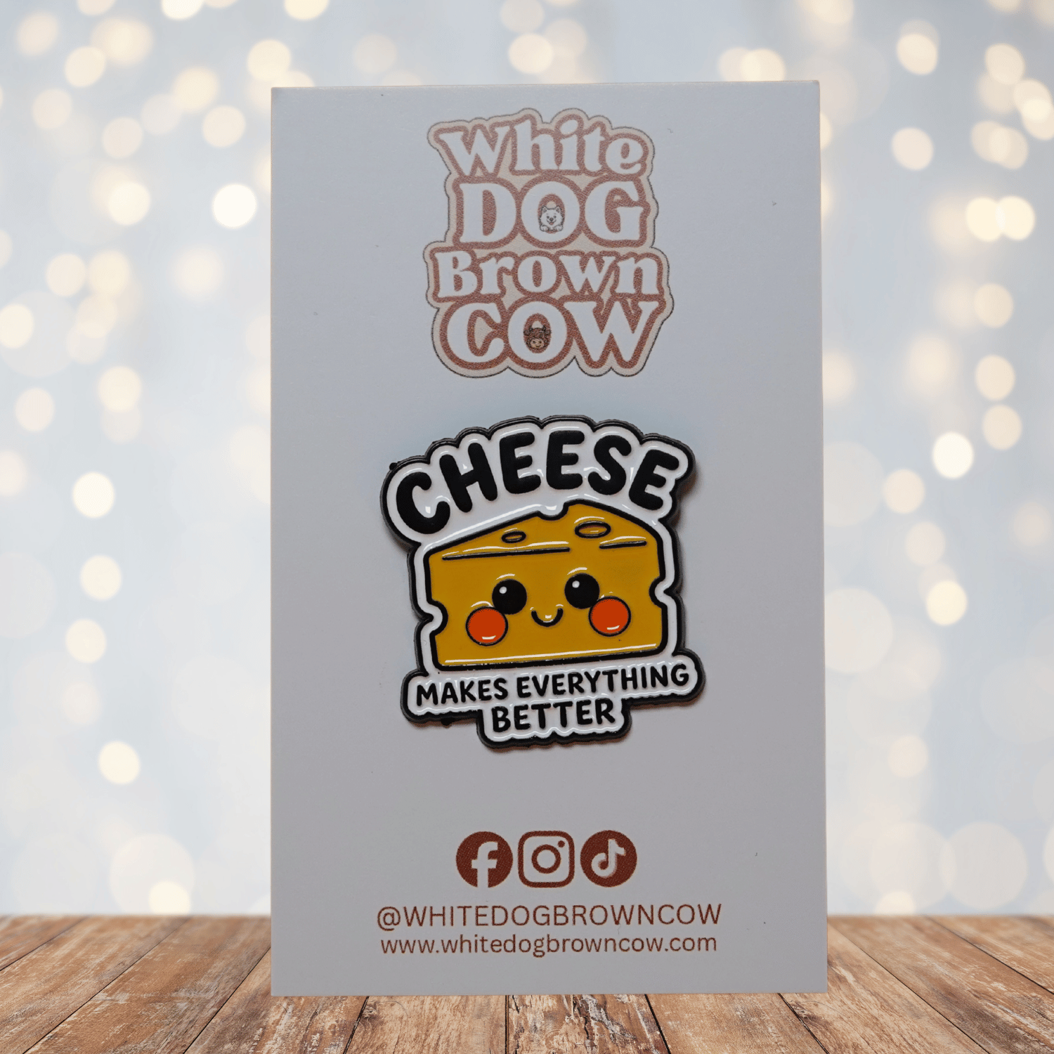 Enamel pin shaped like a smiling yellow cheese wedge with rosy cheeks and the text ‘CHEESE MAKES EVERYTHING BETTER’ on a white background
