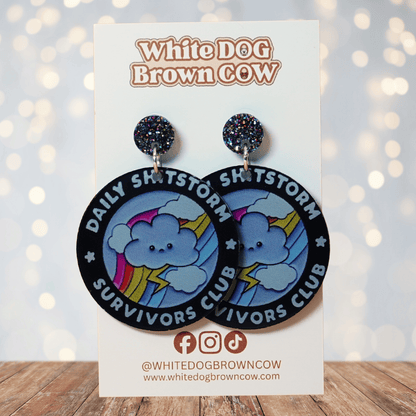 Round novelty dangle earrings reading “Daily Shitstorm Survivors Club” with a cute cloud, rainbow and lightning design