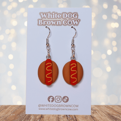 Novelty hot dog dangle earrings shaped like mini hot dogs with mustard detail on a bun and silver hooks.