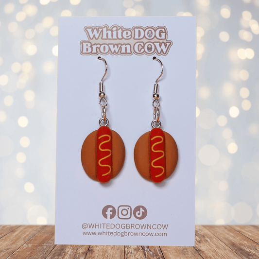 Novelty hot dog dangle earrings shaped like mini hot dogs with mustard detail on a bun and silver hooks.