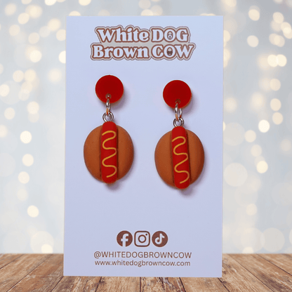 Novelty hot dog dangle earrings shaped like mini hot dogs with mustard detail on a bun and red studs