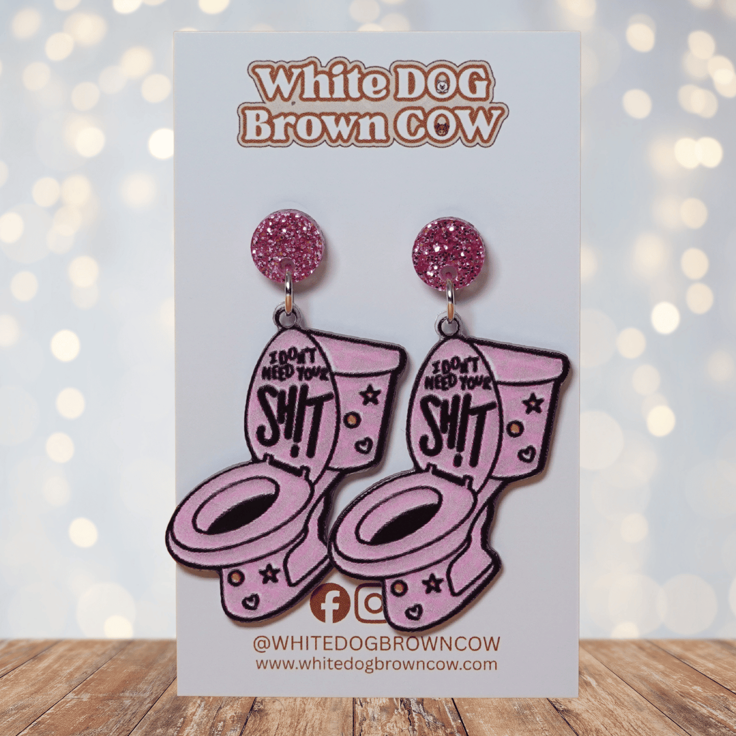 Pink novelty dangle earrings shaped like a toilet with text “I don’t need your sh*t”