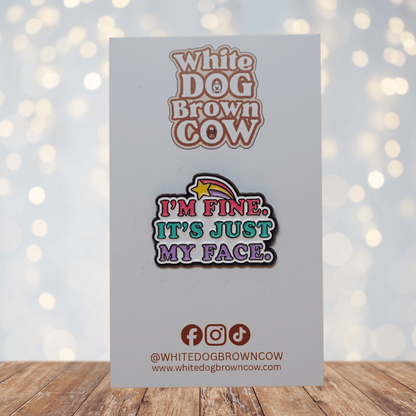 Colorful enamel pin reading “I’m Fine, It’s Just My Face” with retro pink, teal and purple lettering and shooting star detail, funny sarcastic lapel pin.