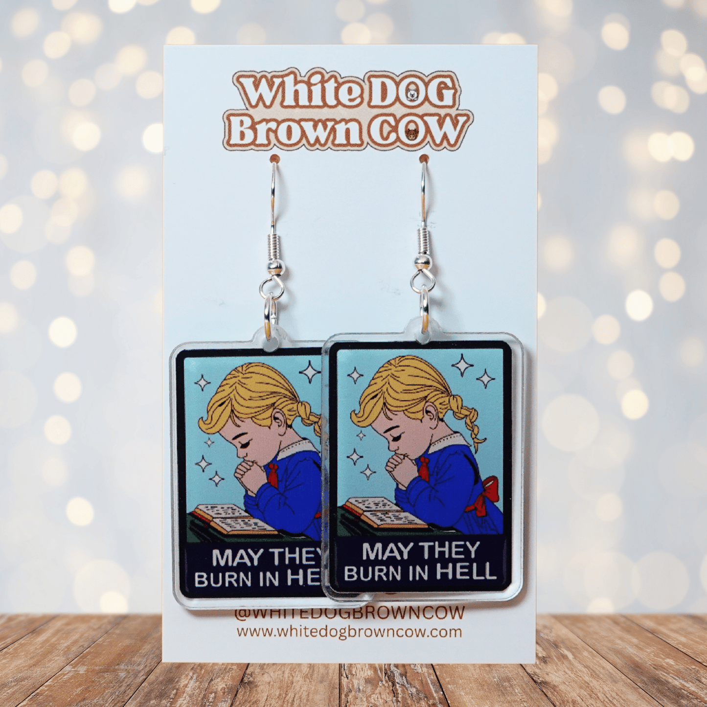Clear acrylic dangle earrings with a vintage illustration of a praying girl and text reading “May they burn in hell”