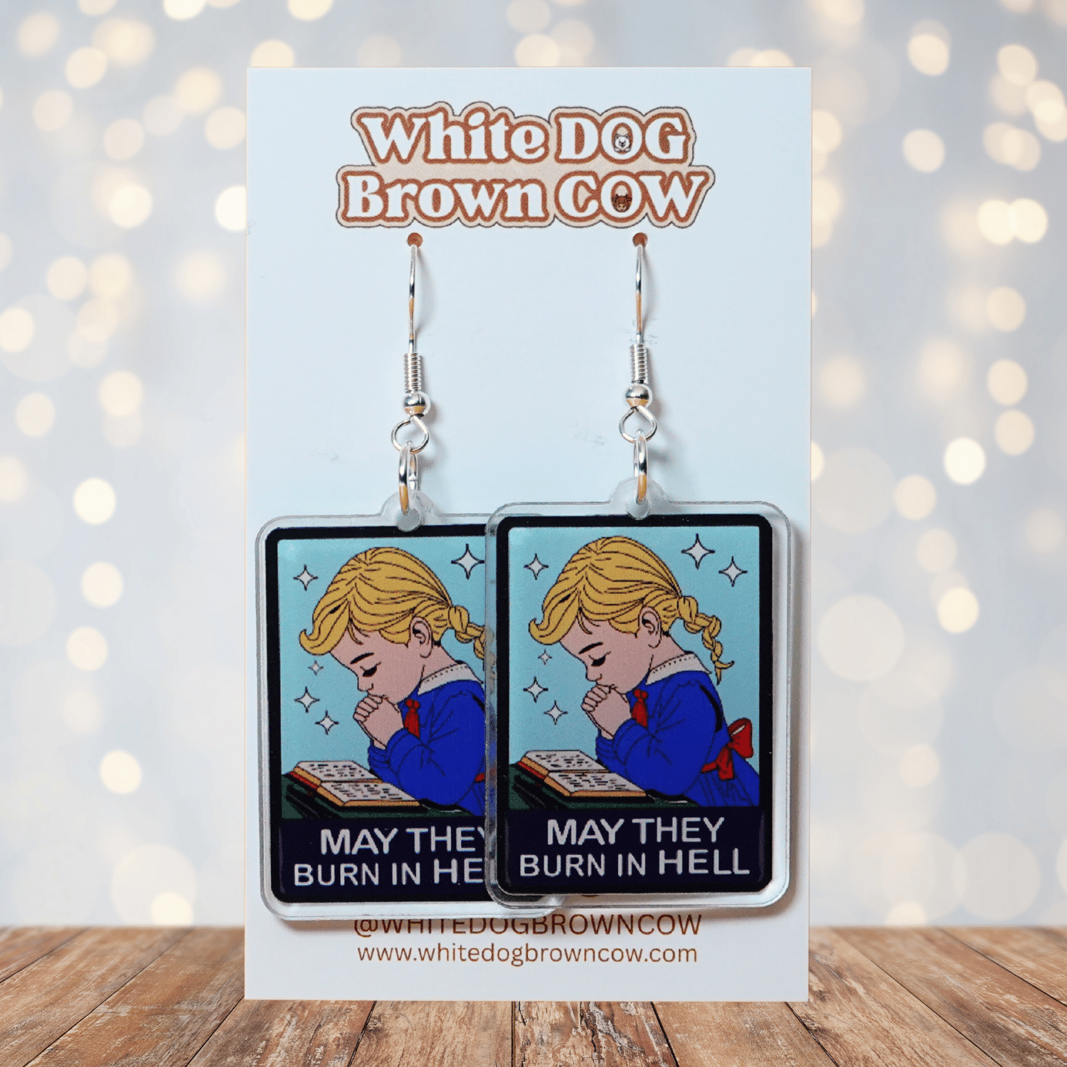 Clear acrylic dangle earrings with a vintage illustration of a praying girl and text reading “May they burn in hell”