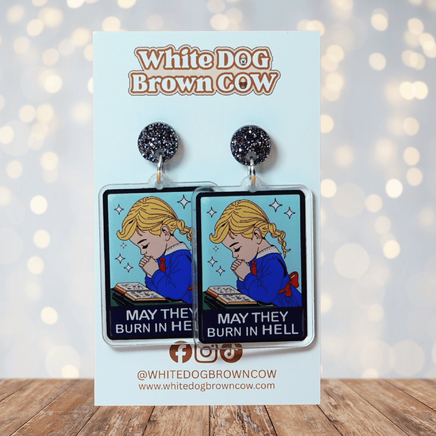 Clear acrylic dangle earrings with a vintage illustration of a praying girl and text reading “May they burn in hell”