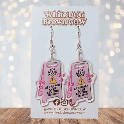 Funny acrylic dangle earrings shaped like a caution sign that reads “Not in the mood – approach with caution,” decorated with small pink hearts.