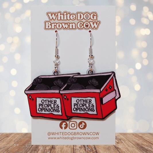 Acrylic dangle earrings shaped like a red dumpster labeled “Other People’s Opinions” with trash bags inside