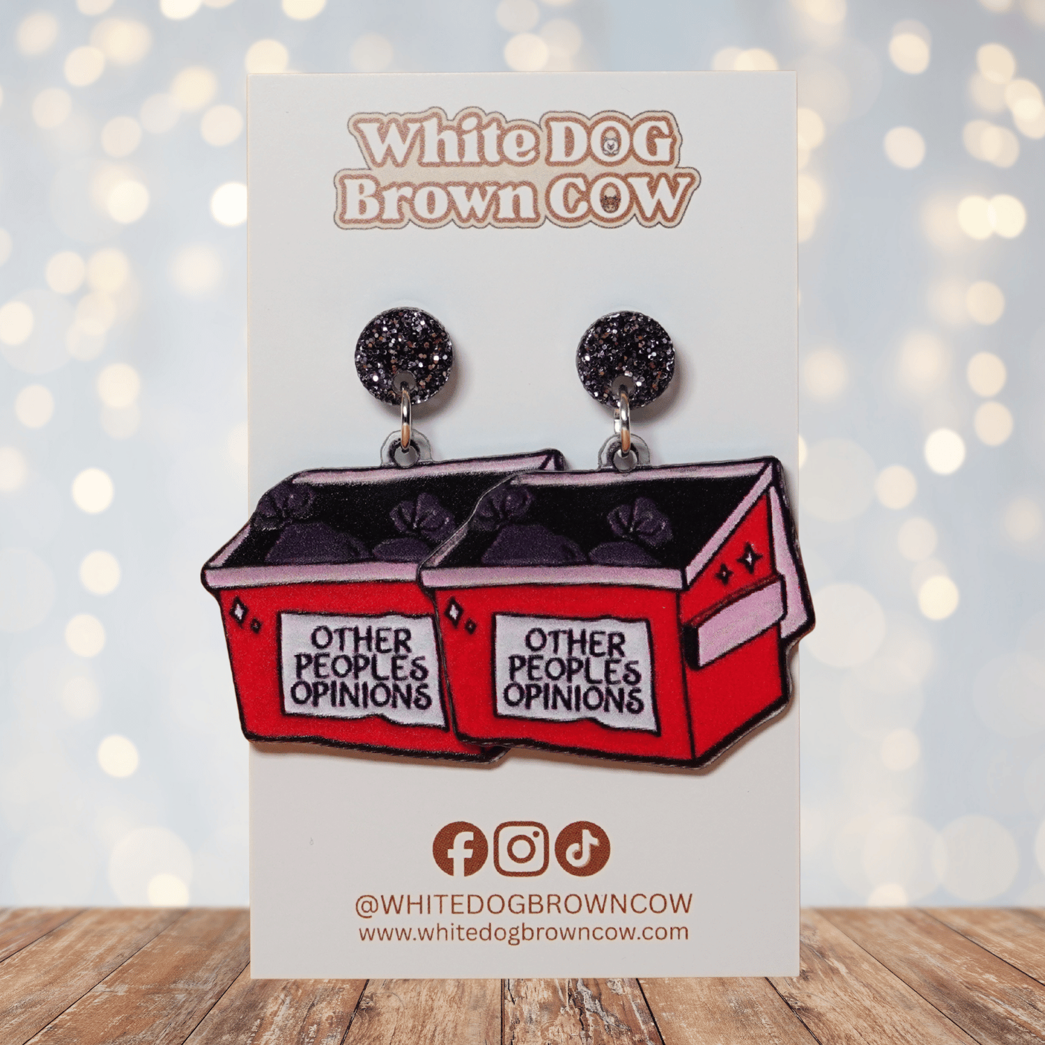 Acrylic dangle earrings shaped like a red dumpster labeled “Other People’s Opinions” with trash bags inside